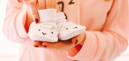 A woman in pink holds cute baby shoes with sheep designs, symbolizing warmth and love.