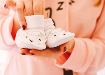 A woman in pink holds cute baby shoes with sheep designs, symbolizing warmth and love.